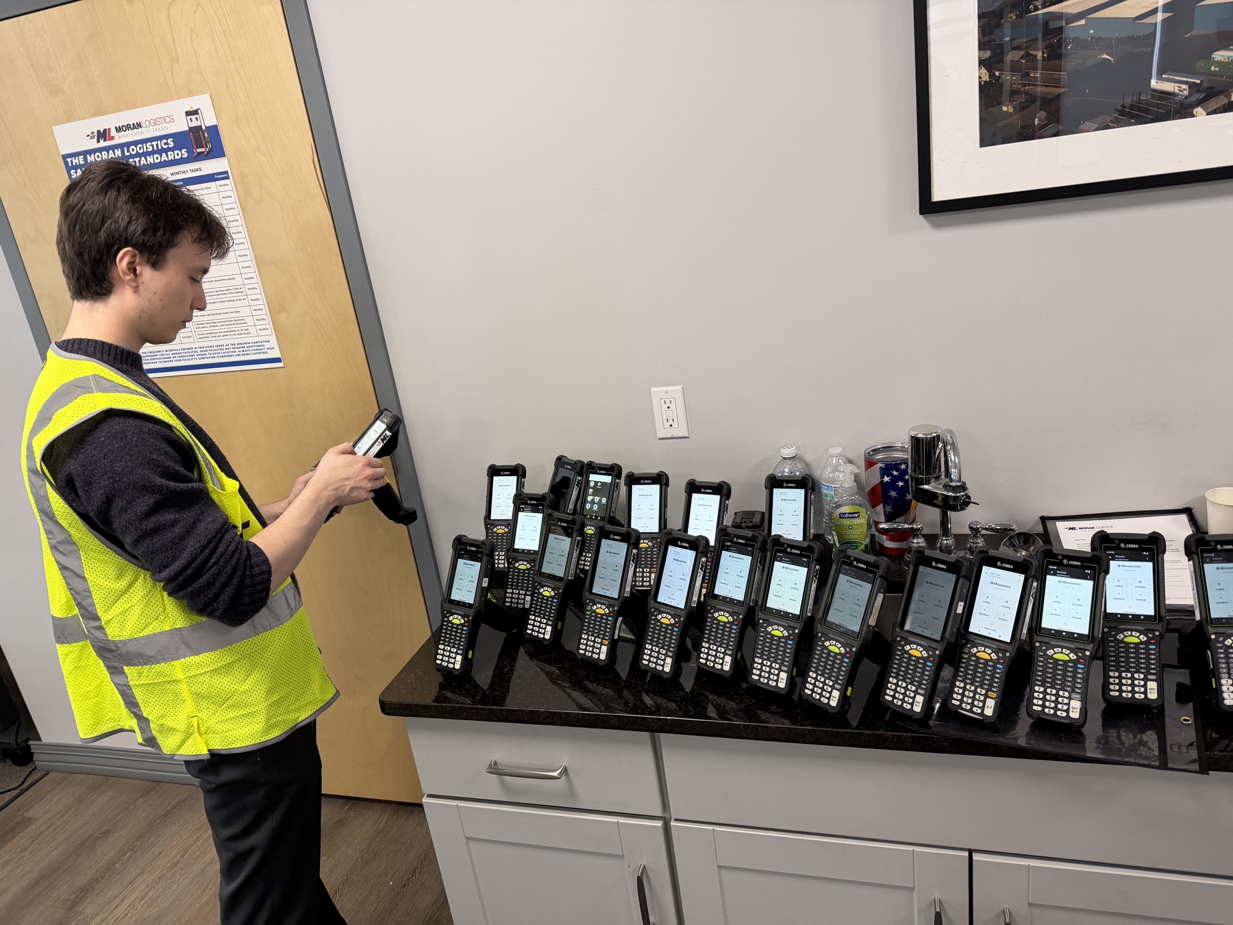 Two dozen RF handhelds lined up on a counter during a facility rollout, each loaded with the same Movo build